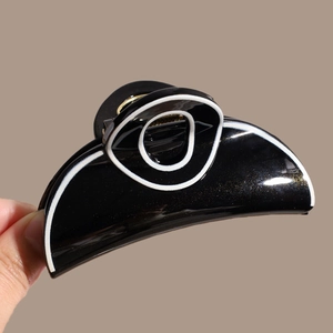 Detail of large black hair claw clip featuring white geometric lines and gold glitter finish