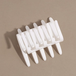 Macro shot of white matte finish hair claw clip for elegant bun styling on brown background