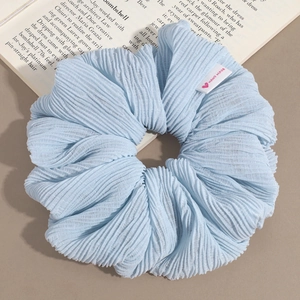 Détail d'un chouchou plissé bleu clair avec une étiquette Hand Made sur fond décoratif