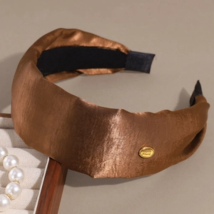 Detail of a brown satin headband with elegant pleats and a gold-tone smile metal tag