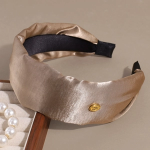 Detail of champagne satin headband with shiny Smile Happy gold metal plaque logo