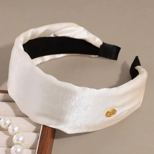 Detailed shot of cream satin headband with golden 'SMILE' button and elegant pleats