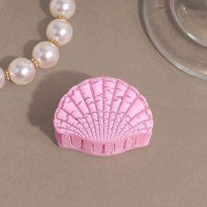 Detail view of pink scallop-shaped hair claw with matte shell texture and pearl decor