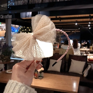 Détail du serre-tête en satin rose orné d'un grand nœud en résille à paillettes dorées
