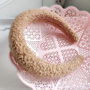 Dettaglio del cerchietto in peluche di agnello color cammello su vassoio rosa