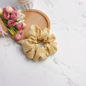 Detailaufnahme von gelbem Karo-Haargummi mit Stofftextur auf einem Holztablett mit Rosen