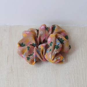 Detailansicht eines floralen Chiffon-Scrunchies mit Pastellmuster auf Holzoberfläche
