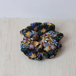 Nahaufnahme eines schwarzen Scrunchies mit buntem Blumenmuster auf hellem Holzgrund