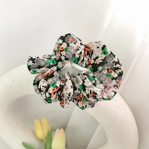 Blumiges Haargummi mit orange-weißen Blüten auf dekorativer weißer Keramikvase