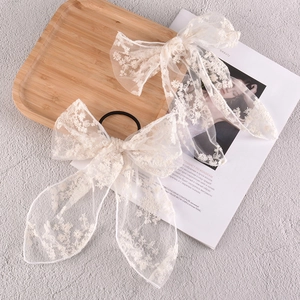 Detail of off-white lace bow hair clips with delicate floral embroidery on chiffon fabric