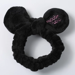 Detail of plush black headband with round ears, bow, and pink embroidery on white background