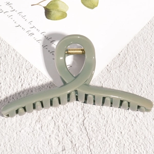 Detail view of a matte sage green hair claw clip with a strong gold metal spring mechanism