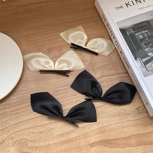Ensemble de barrettes à nœuds en satin noir et beige crème sur surface boisée