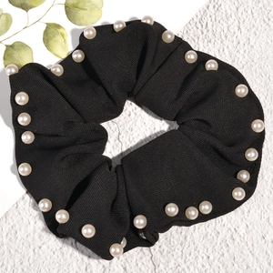 Close-up of black scrunchie with pearl embellishments on a clean textured background