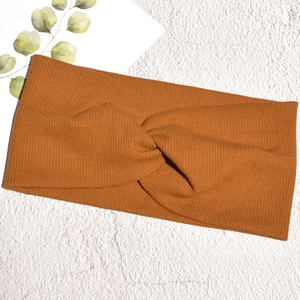 Dettaglio della fascia in maglia a costine color caramello con nodo su sfondo bianco