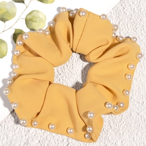 Close-up of bright yellow fabric scrunchie with embedded white pearls on white background