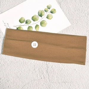 Detail of tan elastic knit headband with white button on a textured stone surface