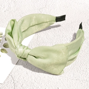 Close-up of light green satin knotted headband with fabric end wraps on stone surface