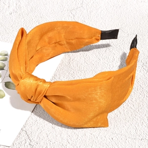 Detail of a shiny orange satin headband with a large bow on a white marble background