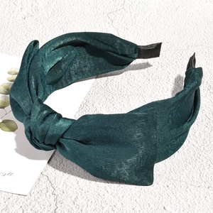 Detail of a dark green fabric headband with a knotted design on a white textured background