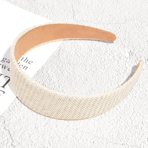 Detailed close-up of a wide raffia braided headband on a minimalist white marble background