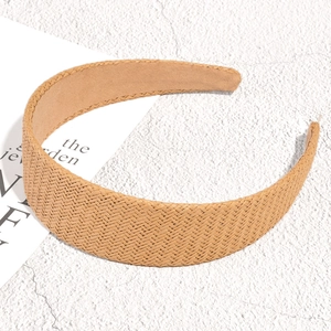 Detail shot of a wide raffia braided headband in natural khaki on a textured white surface