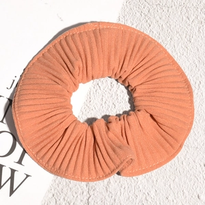 Detailed view of an orange pleated oversized hair scrunchie with vertical stripe texture