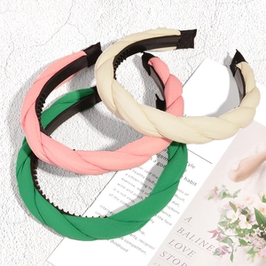 Three braided fabric headbands in pink, cream, and green with non-slip tooth design