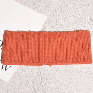 Détail du bandeau en maille orange avec texture côtelée et pompons 3D décoratifs