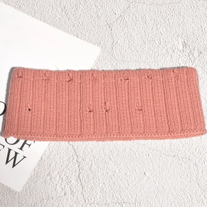 Détail d'un bandeau en tricot rose corail avec texture côtelée et pompons 3D doux