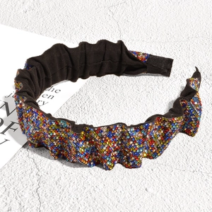 Close-up of pleated headband with colorful rhinestones on a textured background