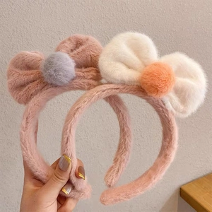 Detail of soft plush bow headbands with fluffy pom-poms in pink and white colors.