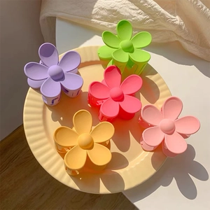 Close-up of five matte flower hair clips in various candy colors on a cream striped plate