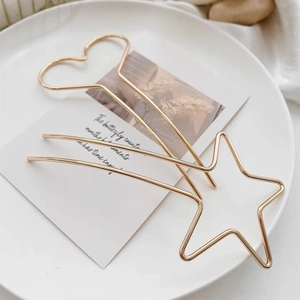 Détail de pinces à cheveux dorées minimalistes en forme d'étoile et de cœur sur blanc