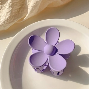 Close-up of a matte purple flower hair claw clip displayed on a ceramic plate
