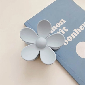 Close-up of a matte light blue flower hair claw clip on a vintage book surface