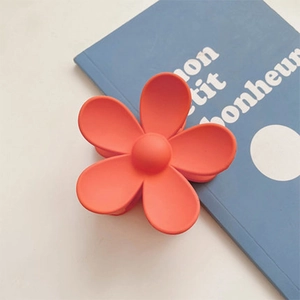 Macro detail of matte orange flower hair claw clip on a light blue decorative book base