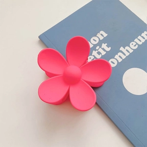 Macro detail of pink matte flower hair claw clip with metal spring on a blue book