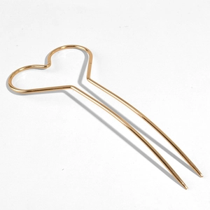 Détail macro d'une épingle à cheveux minimaliste en métal doré en forme de cœur à deux branches