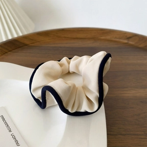 Elegant retro off-white fabric scrunchie with black edging on a rustic wooden table
