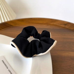 Detail of a black scrunchie with beige wavy edges on a ceramic plate with soft lighting