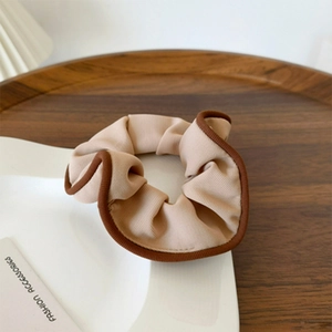 Ribbed fabric scrunchie in beige with brown trim on a minimalist wooden tray