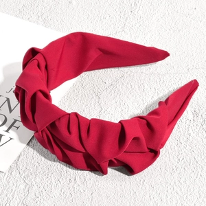 Gros plan détaillé du serre-tête plissé en tissu rouge foncé sur fond texturé blanc