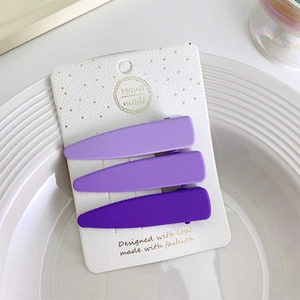 Vista dettagliata di un set di 3 fermagli per capelli viola opachi su carta bianca