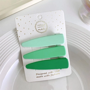 Dettaglio di tre mollette per capelli opache verde sfumato su cartoncino decorato