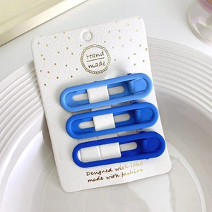 Tre fermagli per capelli opachi blu sfumato su cartoncino in un piatto di ceramica bianca