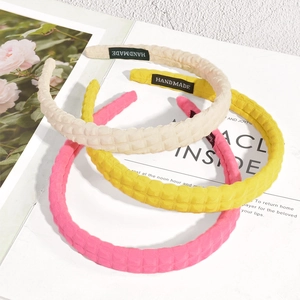 Dettaglio di tre cerchietti a maglia a quadretti in beige giallo e rosa con etichetta fatta a mano