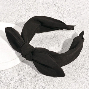 Detailed view of the knotted black bow headband on a textured white display stand