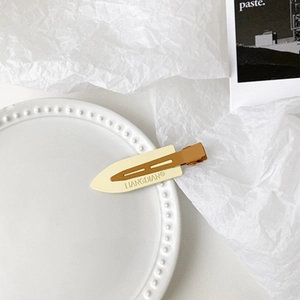 Detailed close-up of matte beige and brown duckbill hair clip on a minimalist tray