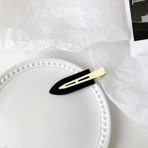 Detail view of a matte black duckbill hair clip with golden metal accents on a ceramic tray